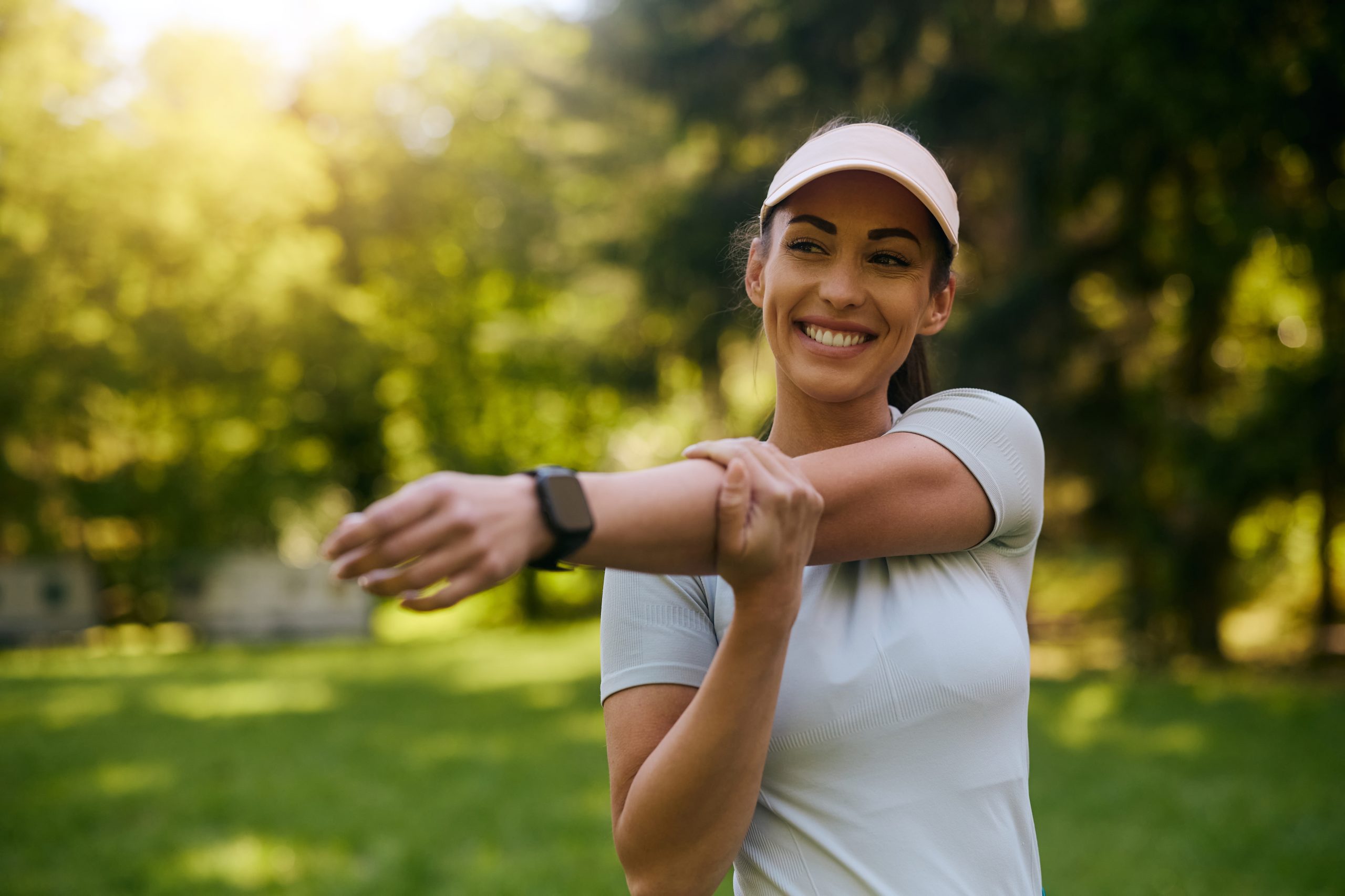 Happy,Sportswoman,Stretching,Her,Arms,While,Exercising,In,The,Park.